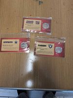 Three sealed Budweiser NFL medallion packs for Giants, Cowboys, Raiders displayed on table