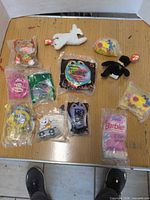 All 12 toys laid out on tabletop showing sealed bags and two plush