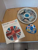 Overall lot view showing round tray, triangular plate, Britain brochure cover