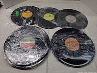 Group of six plastic-wrapped vinyl records showing centre labels