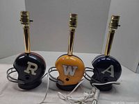Front view of three football helmet lamps showing team letters and colors