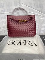 Front view of burgundy woven tote showing gold knot hardware