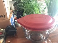 Side view of clear glass bowl with red lid on tabletop