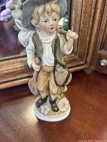 Small boy figurine with hat, bag, mandolin, flowers on base