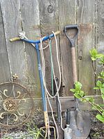 Blue T-handle tool, shovel, trowel and circular metal plaque against fence