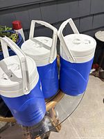 Three blue Coleman insulated water jugs on glass table