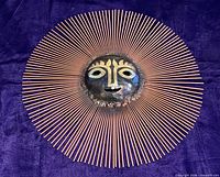 Full view of mixed metal sun sculpture showing copper rod rays and central face