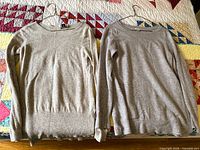 Both grey cashmere sweaters on hangers side by side