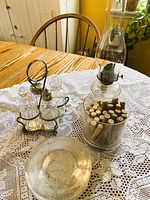 Cruet set, oil lamp, jar of clothes pins, dessert plate on lace tablecloth