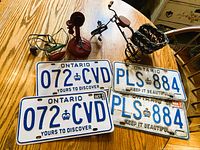 All items grouped on table: candlestick phone, toy iron, miniature bicycle, four Ontario licence plates