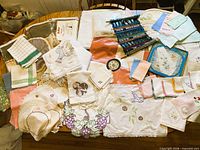 Overview of table covered with assorted linens, doilies, towels, curtains, runner