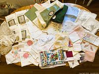Overview of all assorted linens spread on table showing packaged curtains, crochet, embroidery, hankies