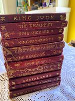Stacked view of 12 red leather Temple Shakespeare books showing gilt spine titles