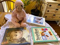 Porcelain doll seated beside three reference books on lace cloth