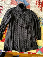 full view of black cable-knit turtleneck sweater laid flat