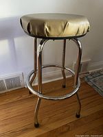 Full view of chrome bar stool, beige vinyl seat, hardwood floor