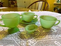 Group shot of all jadeite items: two Fire-King cups, saucer, Fenton handled cup, oval dish