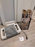 Rectangular HoMedics Therapist Select shiatsu massager with handles and power cord alongside open box for Thera-P handheld massager