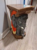 Front view of ceramic elephant stool, showing elephant head, tusks, blanket and top surface