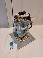 Front view of silver glitter head sculpture with jewelry adornments on square base