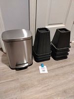 pedal trash can beside two stacks of black furniture risers
