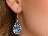 Earring worn on ear showing pear-cut blue topaz drop in 10K gold setting
