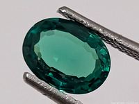 Front view of oval faceted synthetic emerald held in tweezers