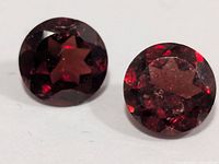 Two round faceted deep red garnet gemstones on white background