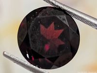 Close-up of round faceted garnet held in tweezers showing color and cut