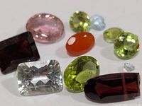 Loose faceted gemstones arranged on white background showing assorted colors and cuts