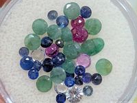 Top view of mixed loose gemstones on white foam inside clear container