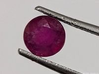 Round faceted ruby held by tweezers front view