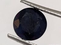 Close-up of round faceted dark blue sapphire held by tweezers