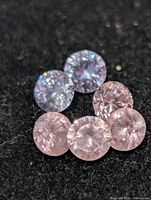 Six loose round-cut CZ stones in light blue and pink on dark background