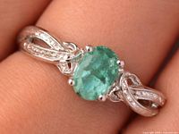 Ring on finger showing emerald center and twisted accent stone shank