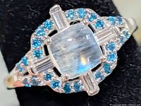 Angled view of sterling silver ring with cushion moonstone and blue CZ halo