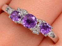 Close-up of ring on finger showing three amethysts and accent stones