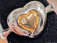 Front view of silver ring with gold-tone heart inset and diamond accent