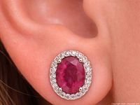 Earring on ear showing size, oval ruby center, halo of clear stones
