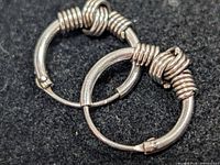 Pair of silver wire-wrapped hoop earrings on dark fabric background