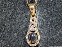 Front view of gold-tone pendant with black opal centre and clear stone border