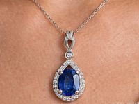 Pendant on chain showing blue sapphire, halo of clear stones, silver setting