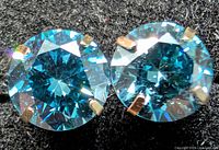 Close-up of both blue diamond stud earrings in 14K gold four-prong settings