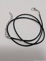 Full view of black cord necklace coiled showing clasp and extender