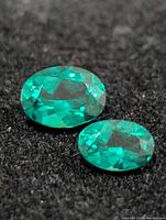 Two oval green faceted gemstones on black background