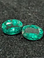 Two oval-cut green gemstones on black background