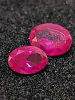 Two oval faceted rubies on dark fabric background