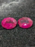 Two oval faceted rubies side by side on black background, showing overall appearance and color