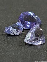 Three faceted violet-blue tanzanite gemstones on dark surface showing chips