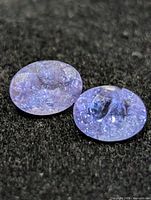 Two oval violet-blue tanzanites on dark background, showing chips and inclusions